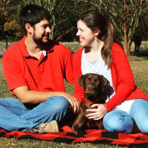 Husband and wife smiling at each other with chocolate lab puppy between them