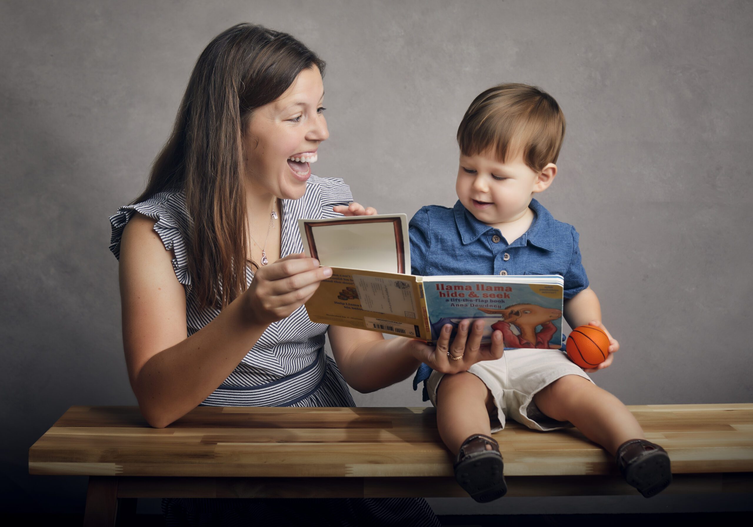 Picture of woman reading llama book to her toddler son who is holding a small basketball